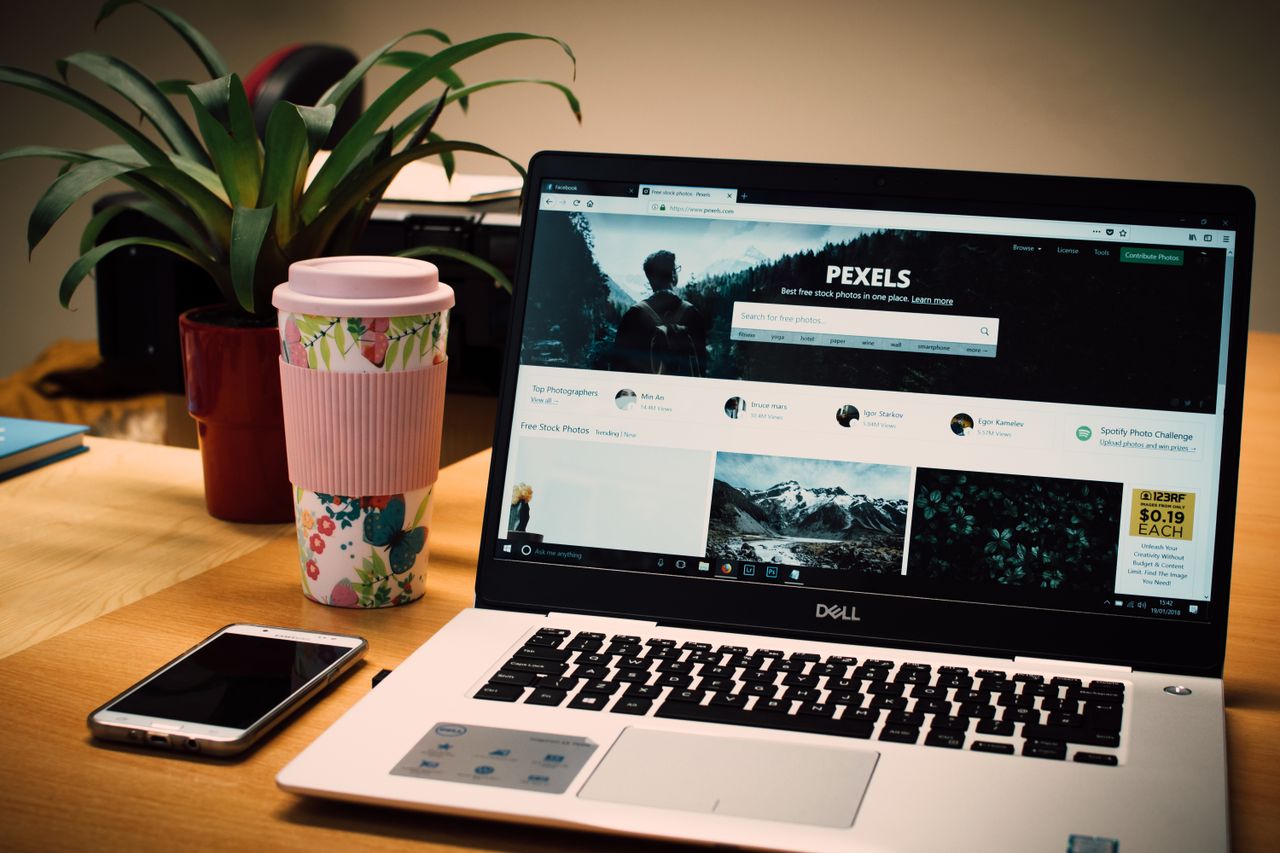 Un bureau bien rangé avec un ordinateur portable affichant un site de photos d’archives et un smartphone.